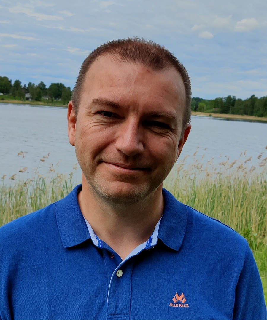 André Martinsen, photographed outdoors in summer in front of a lake and reeds, wearing a blue polo shirt.